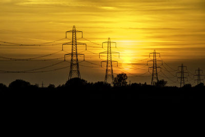 Silhouette electricity pylons on field against orange sky