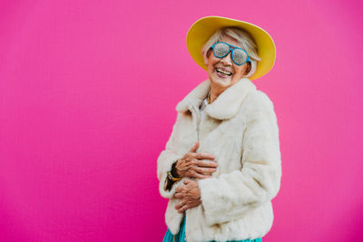 Portrait of smiling woman standing against pink background