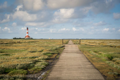 Road leading towards lighthouse on field against sky