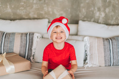 Portrait of cheerful boy with gift box sitting on bed