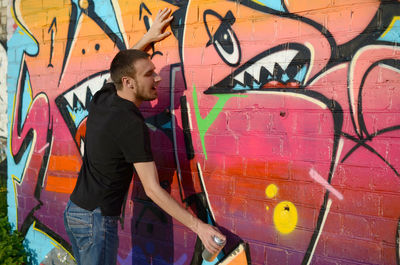 Full length of young man standing against graffiti wall