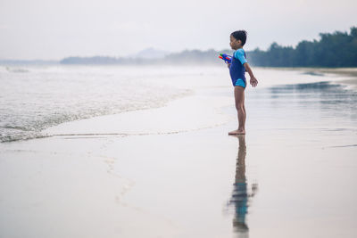 Boy playing with toy at beach against sky during foggy weather
