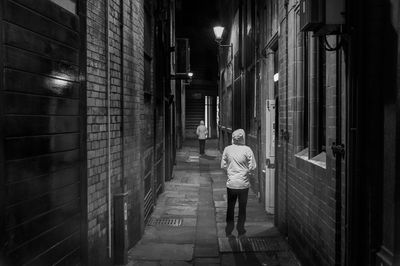 Rear view of man walking on illuminated street amidst buildings