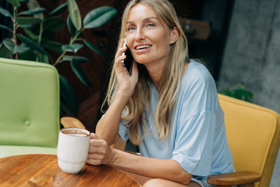 Happy beautiful woman sitting at a table in a coffee shop friendly talking on a mobile phone.