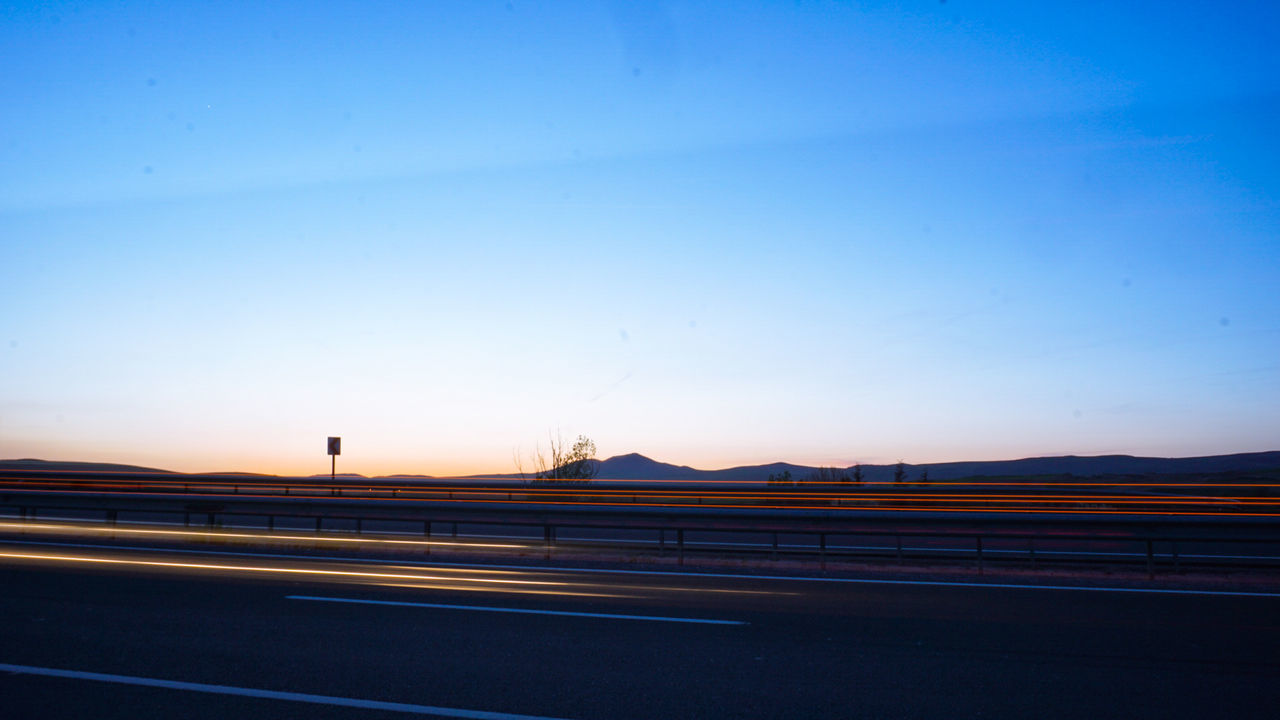 LIGHT TRAILS ON ROAD AGAINST SKY AT SUNSET