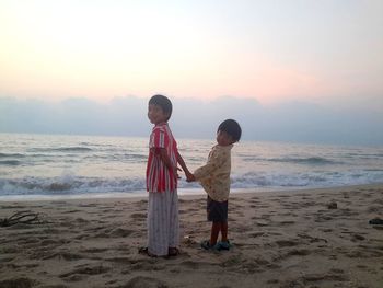 Boy standing on beach against sky during sunset