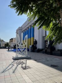 Chairs on sidewalk by building in city against sky