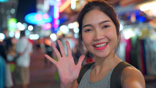 Portrait of smiling young woman standing on street in city at night