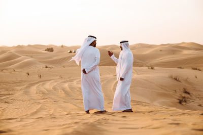 Rear view of men on sand dune in desert against sky