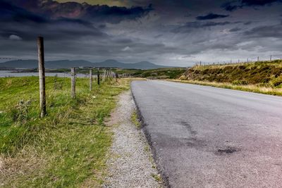 Empty road amidst field against sky