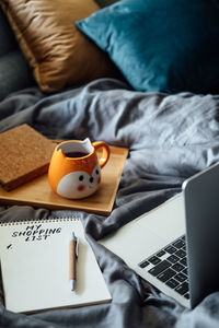 Frugal living tips, save money concept with shopping list in notebook near laptop and tea coffee