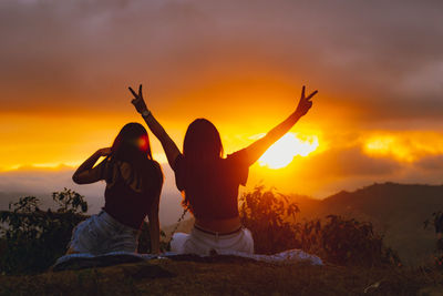 Friends sitting on land against sky during sunset