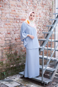 Portrait of young woman standing against brick wall