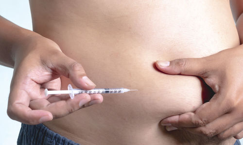 Midsection of shirtless man injecting stomach while standing against white background