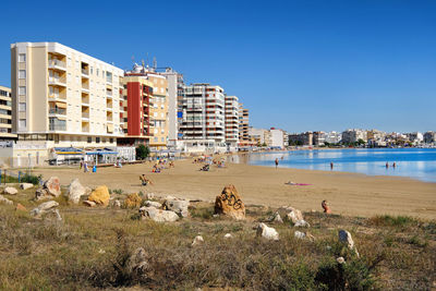 People by sea against clear blue sky