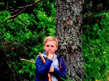 Portrait of cute boy with finger on lips standing against tree