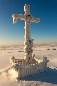 Cross on snow covered land against clear blue sky