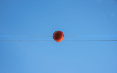 Low angle view of cables with orange equipment against clear blue sky