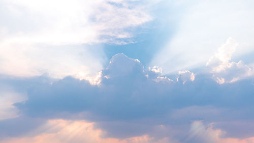 Low angle view of sunlight streaming through clouds