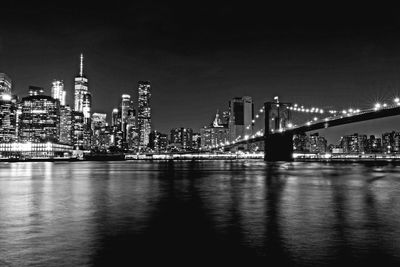 Illuminated bridge over river by buildings against sky at night