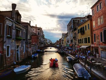 People on canal amidst buildings in city against sky