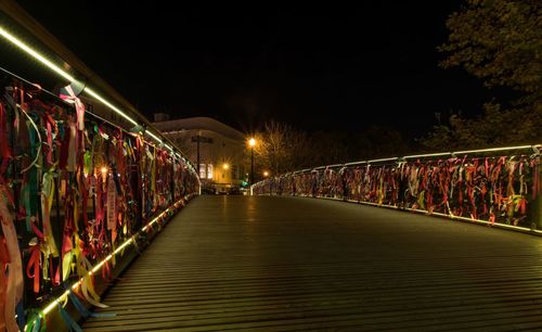 Illuminated footbridge over city against sky at night