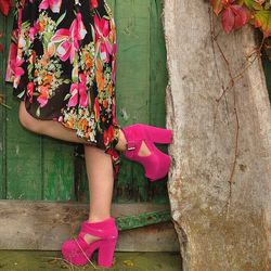 Low section of woman wearing pink heels standing by wooden door