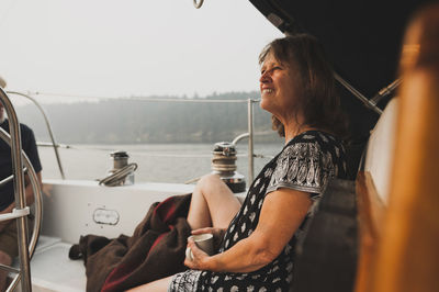 Side view of woman looking away while sitting in boat on sea against sky