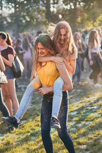 Teenage girl giving friend piggyback ride while standing outdoors