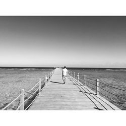 Rear view of man standing on pier at sea against clear sky