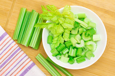 Fresh chopped celery slices in white bowl with celery sticks on bamboo cutting board