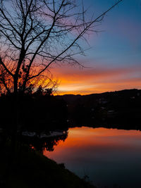 Silhouette trees by lake against romantic sky at sunset