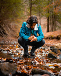 Full length of young man crouching on rock in forest during autumn