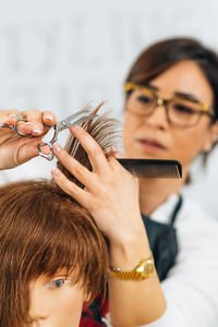 Hairdresser educator with students, explaining hair cutting technique on mannequin head for training