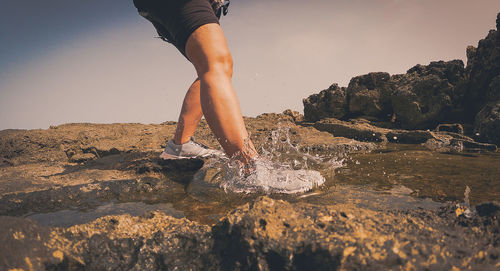 Low section of person on rock at beach against sky