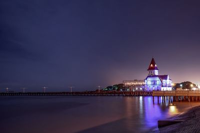 Illuminated club de pescadores by river against sky at night