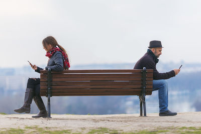 People using smart phones while sitting on bench at observation point