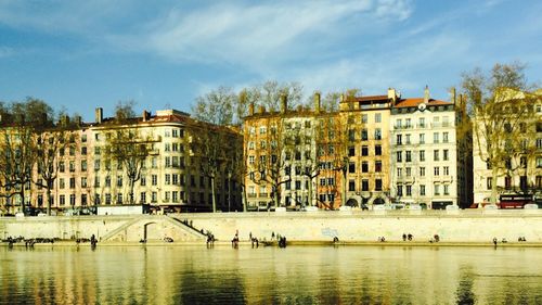 Buildings by river against sky in city