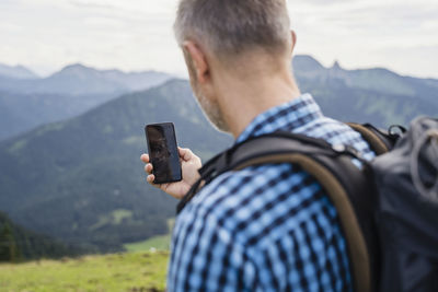 Male backpacker searching direction through navigational compass using mobile phone while hiking