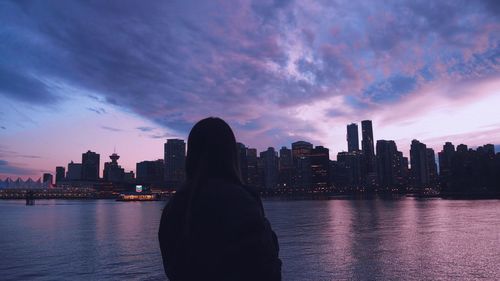 Silhouette buildings by river against sky during sunset