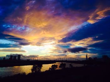 Silhouette bridge over river against cloudy sky during sunset