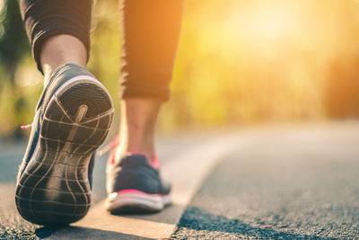 Low section of woman wearing sports shoes while walking on road