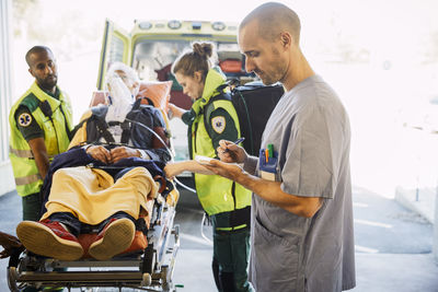 Male nurse writing report while paramedics pushing patient on gurney in hospital