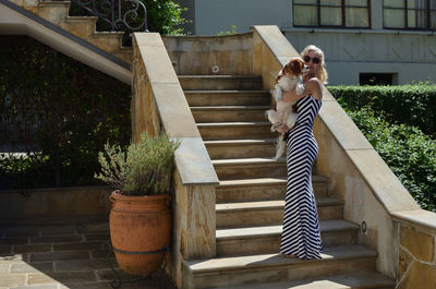 Lady in elegant dress holding her adorable pet cavalier king charles spaniel in mediterranean yard