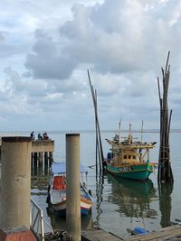 Fishing boats moored at harbor against sky