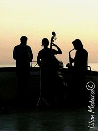 Silhouette men standing by text on road during sunset