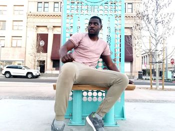 Portrait of young man sitting on seat in city