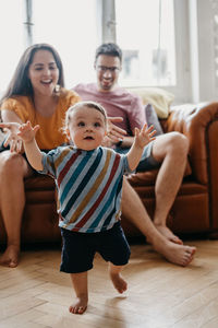 Baby boy walking while parents sitting on sofa at home