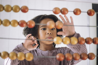 Girl with curly hair learning to count using abacus in classroom at kindergarten