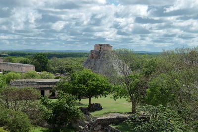 Built structure by trees against cloudy sky